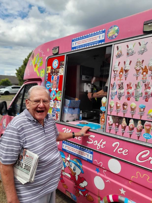 older man standing next to a pink ice cream truck smiling